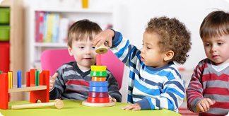 Three children playing with a ring stacker in a nursery