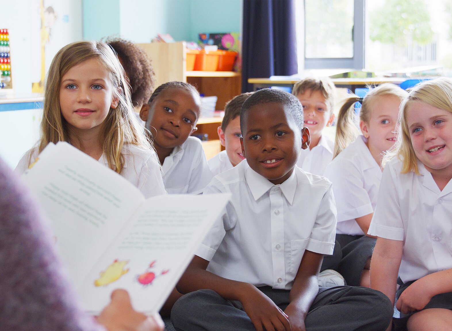 Primary aged students sat on the classroom floor, listening to the teacher read a book