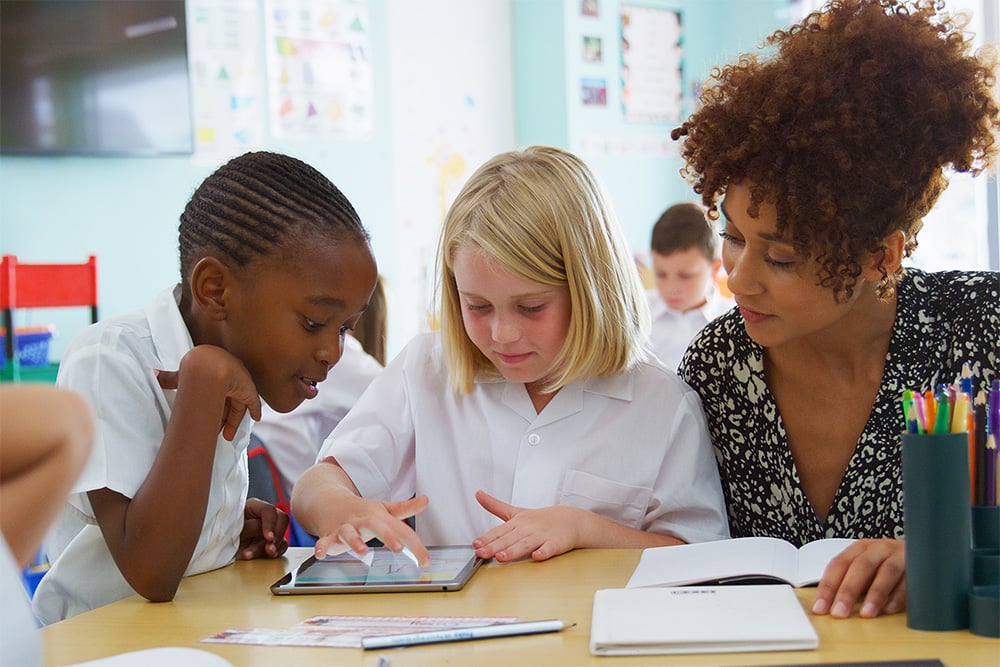 A primary teacher with two pupils working on an exercise at a desk
