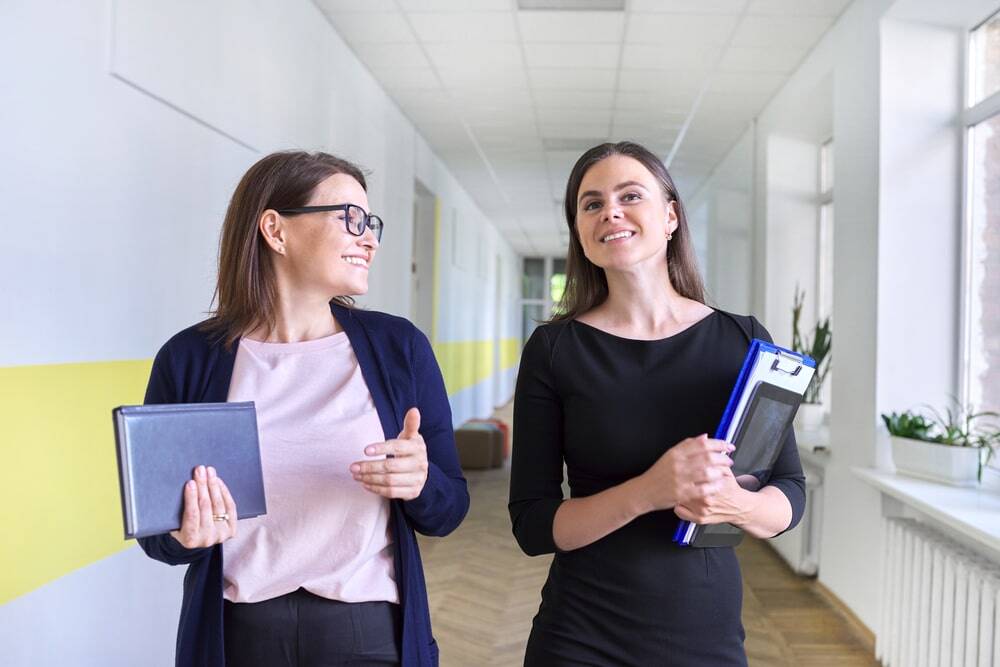 Two female school staff members walking down the school hallway smiling